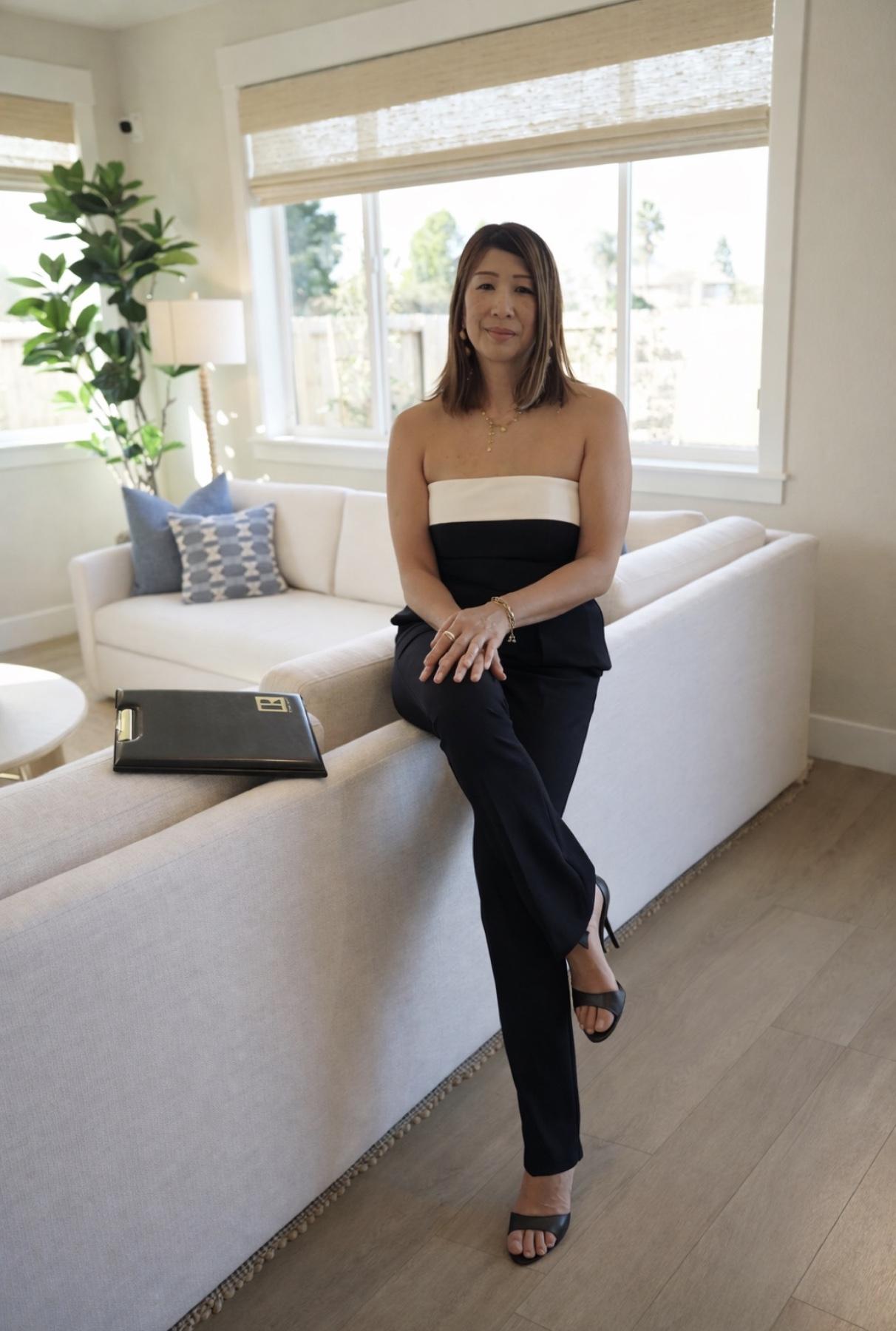 Helen Wong seated on the arm of a cream sofa in a bright living room, a Premier Realty folder beside her